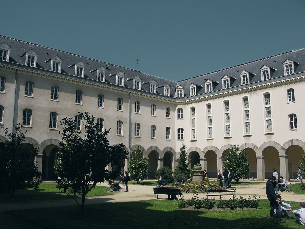 Le cloître de la Faculté des sciences économiques de Rennes : un jardin bordé d’arcades en pierre, entouré de bâtiments à toits d’ardoise, avec des étudiants sur les pelouses.